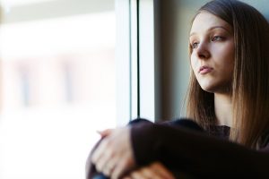 窓際で体育座りする虚ろな女性