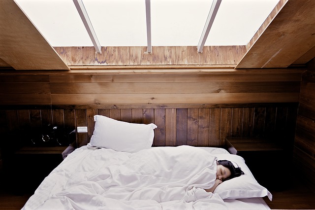 天窓の下のベッド。白いシーツに包まり、横たわる女性