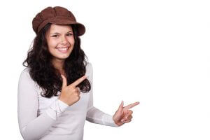 両手の指で銃の形で左を指す茶色の帽子をかぶるソバージュの笑顔の女性