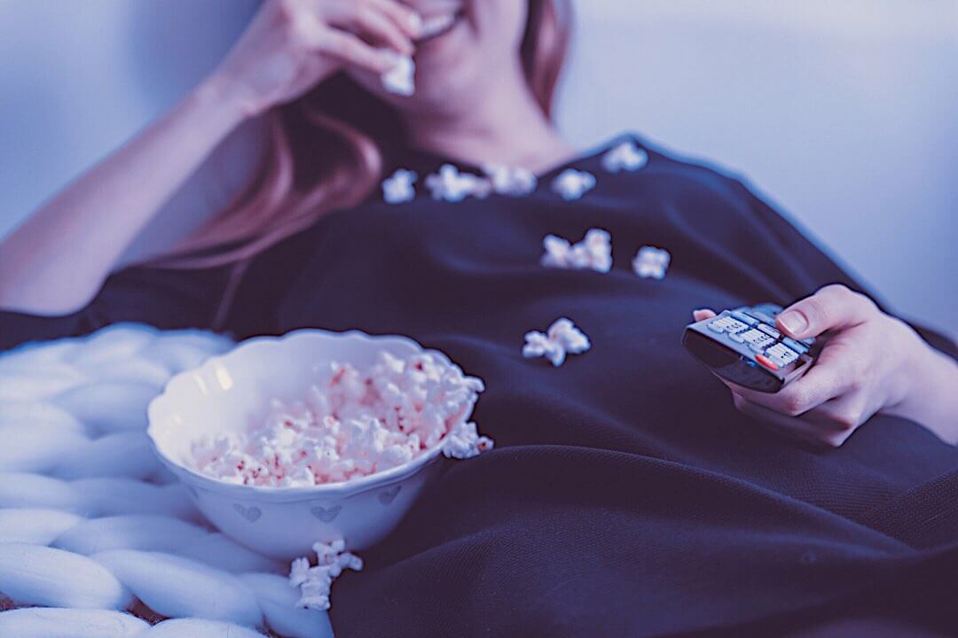 横になってテレビを見ながらポップコーンを食べ散らかす、紺色の服の女性