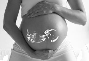 妊婦さんがお腹の上下に手を添えている。お腹に赤ちゃんの影が映る